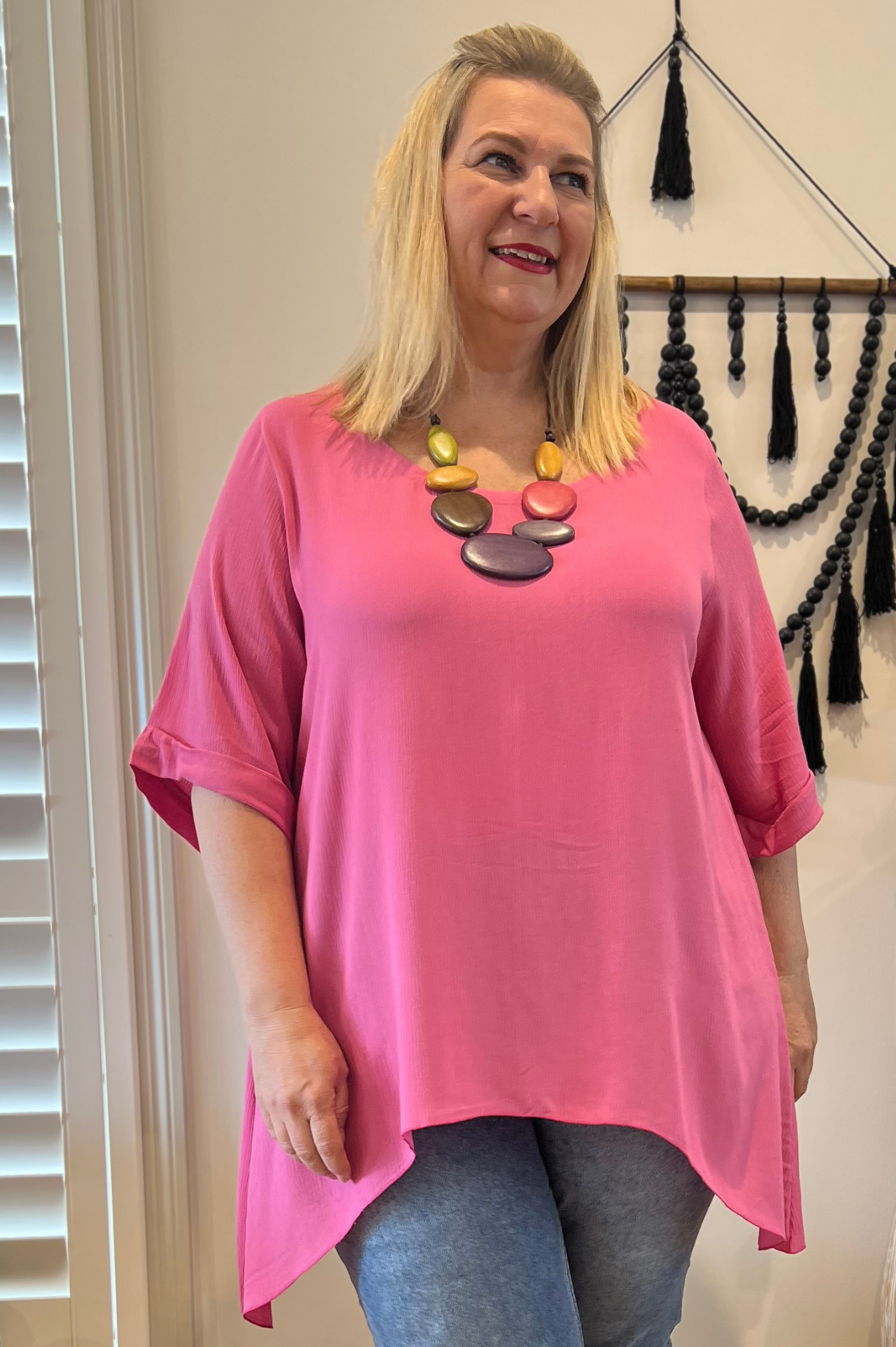 Kita Ku modelling a pretty pink scoop shaped top with a colourful necklace in a lounge setting. 