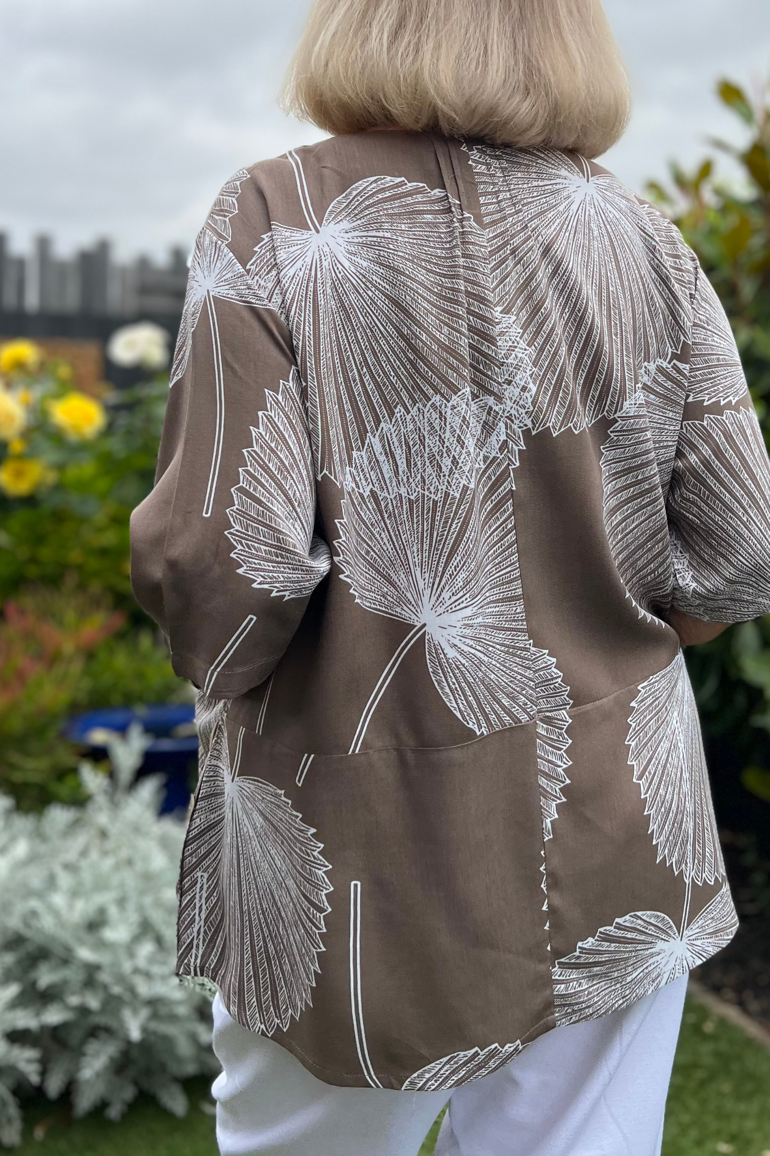 Kita Ku model wearing a mocha and white large fan palm leaf printed top over white pants