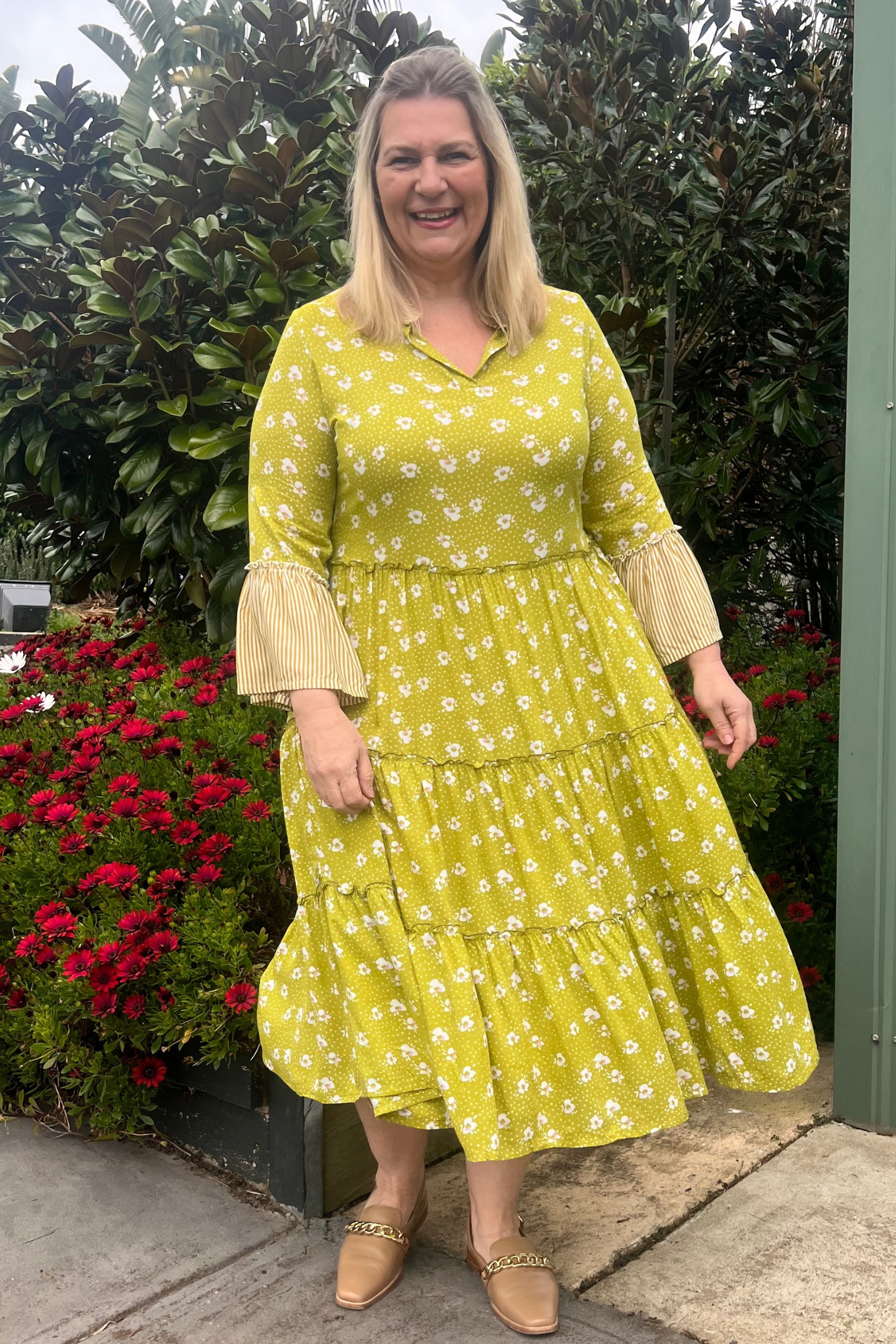 Kita Ku modelling a chartreuse floral layered dress in a garden setting. 
