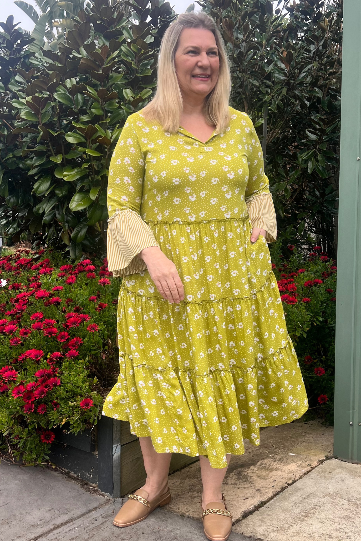 Kita Ku modelling a chartreuse floral layered dress in a garden setting.