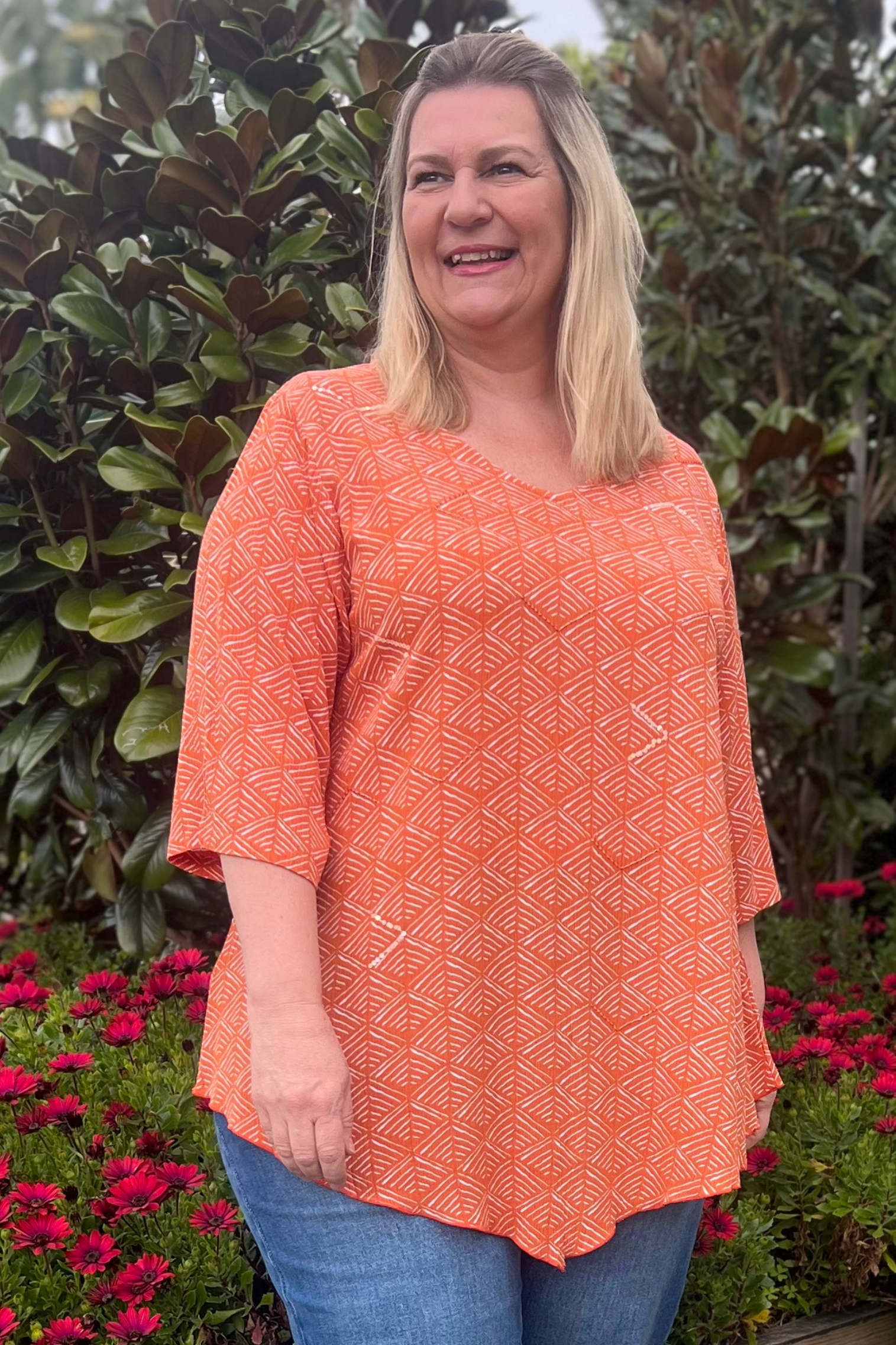 Kita Ku modelling an orange abstract printed top with some sequins embellishments in a garden setting. 