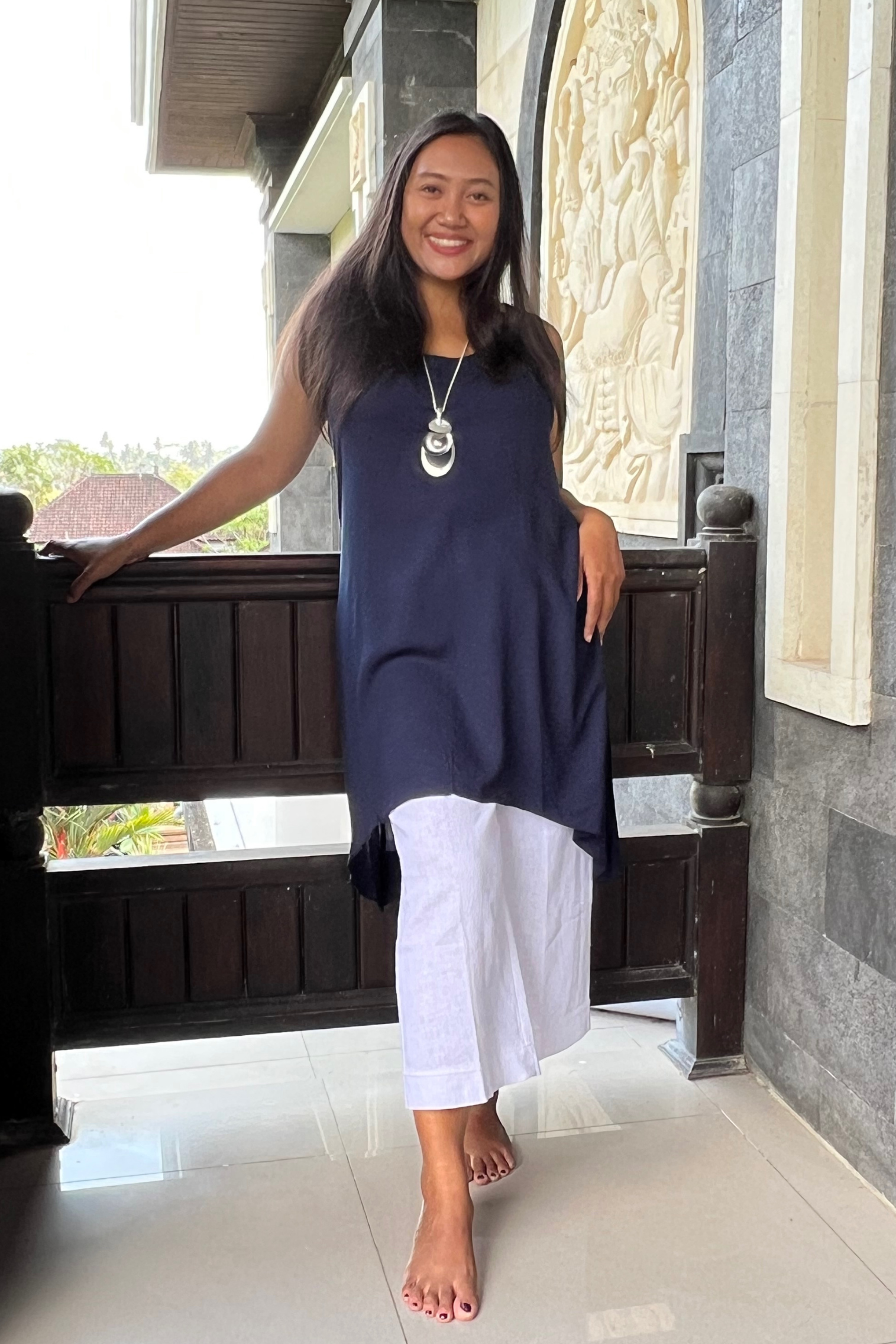 kitaku model wearing a navy long scoop tunic axel over white cotton pant in a Balinese setting.