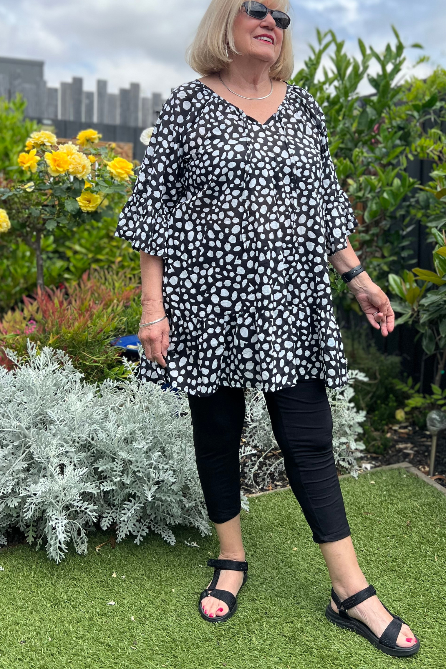 Kita Ku modelling the black 3/4 stretch legging, with a black and white cotton top in a garden setting. 