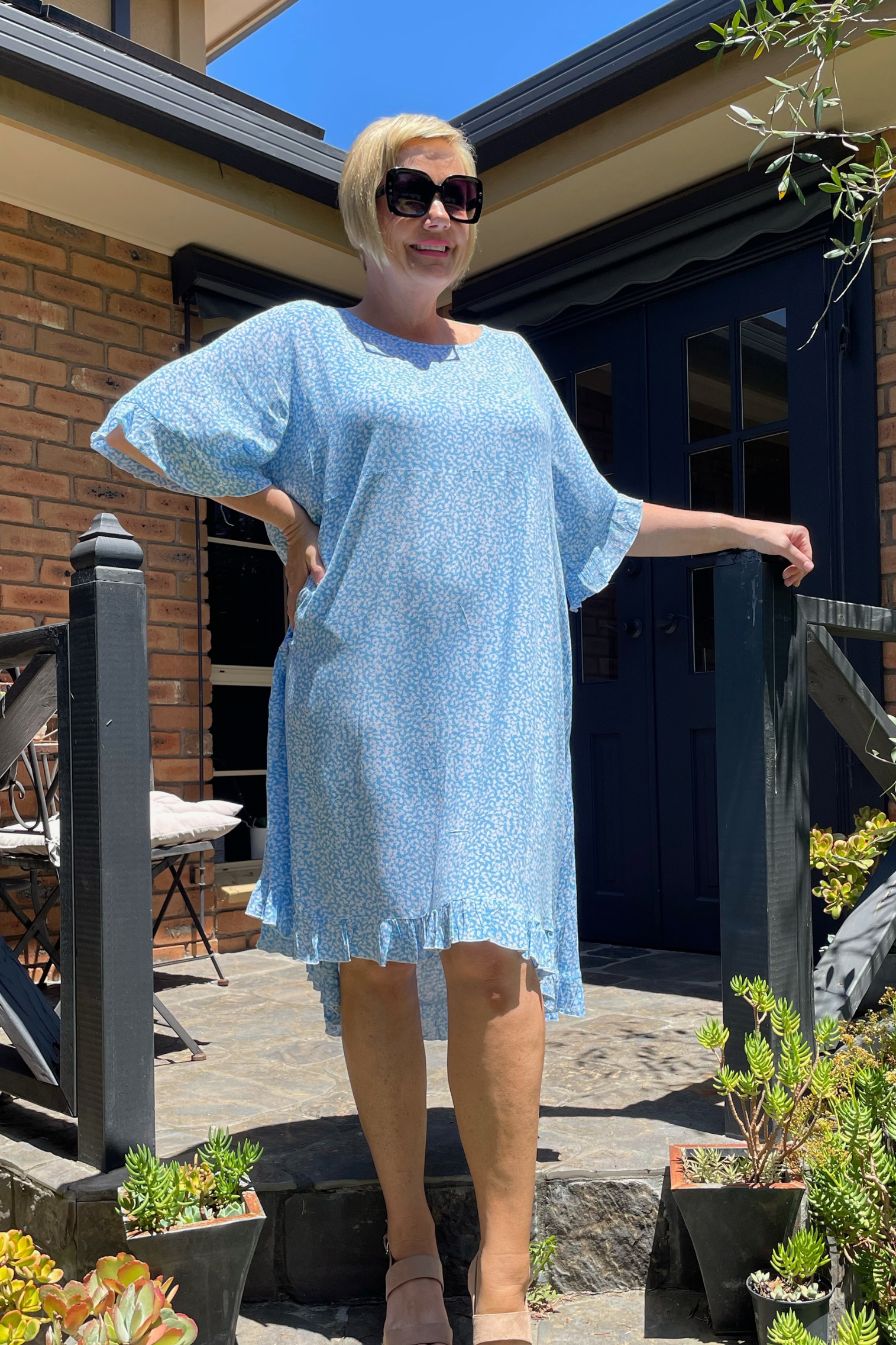 Kita Ku plus size dress Leonie in a pretty soft blue and white holly print, set in a sunny garden.