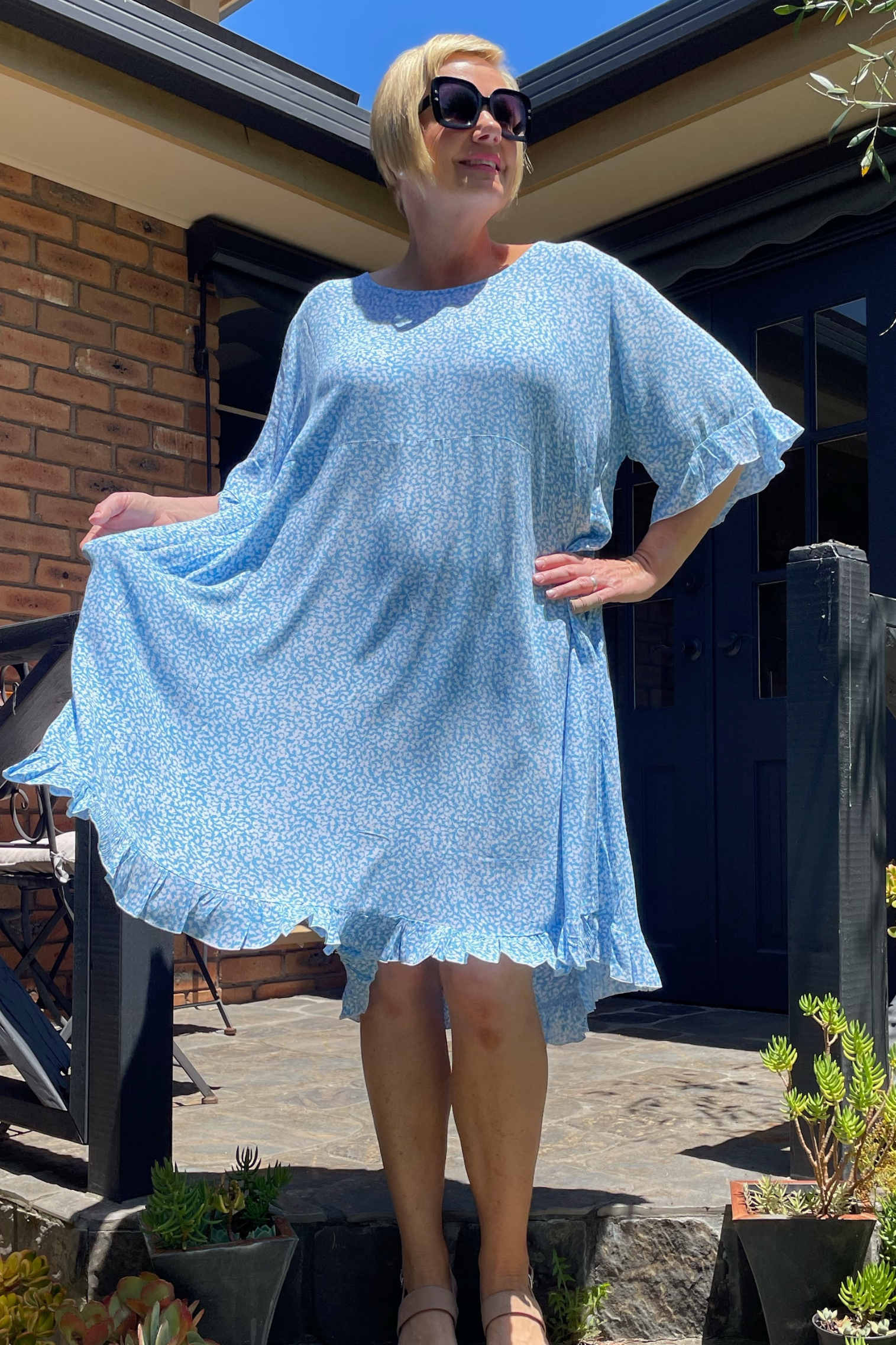 Kita Ku plus size dress Leonie in a pretty soft blue and white holly print, set in a sunny garden.