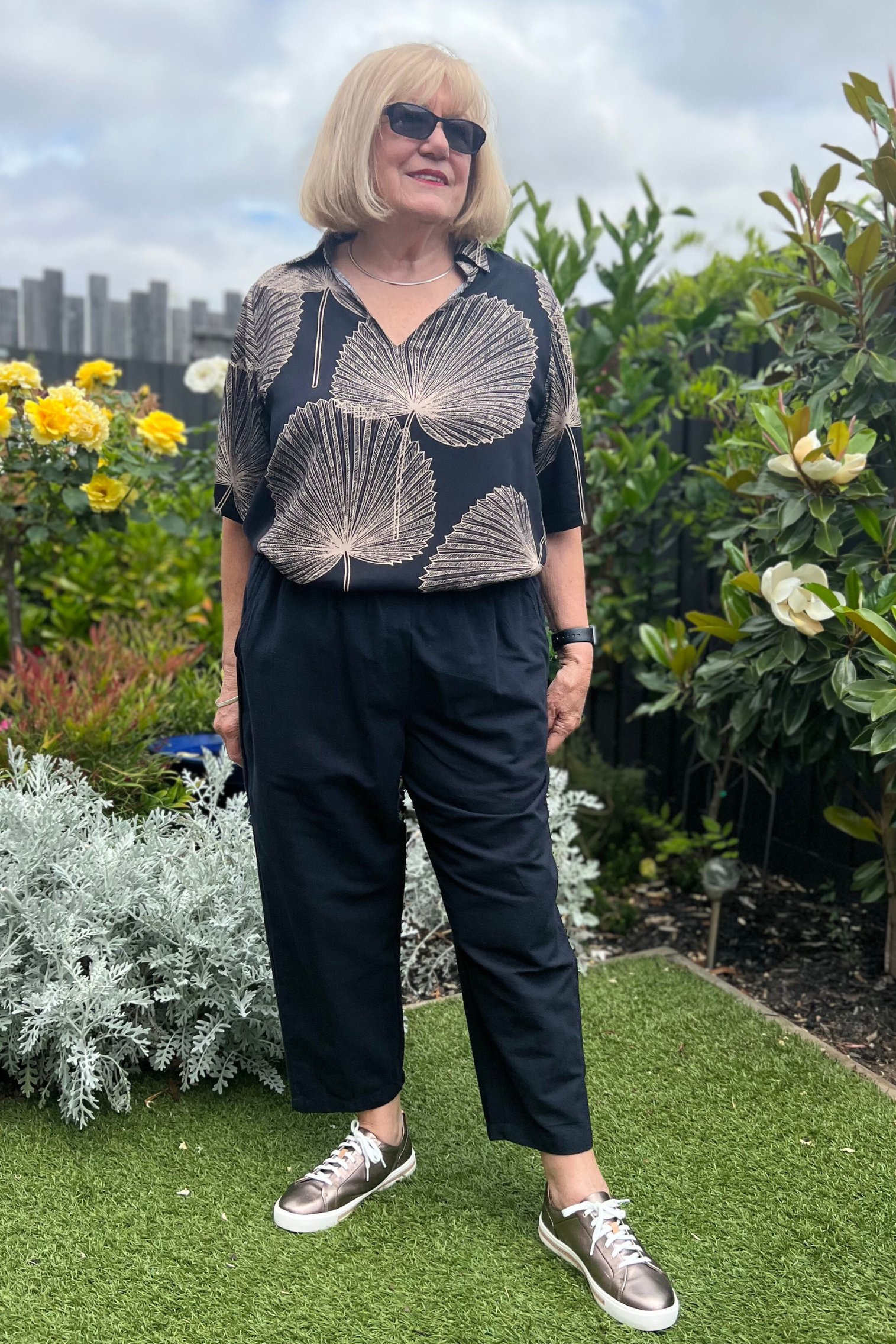 Kita Ku modelling the cotton black pant port with a top rebecca in Paolo print, and set in a sunny garden.