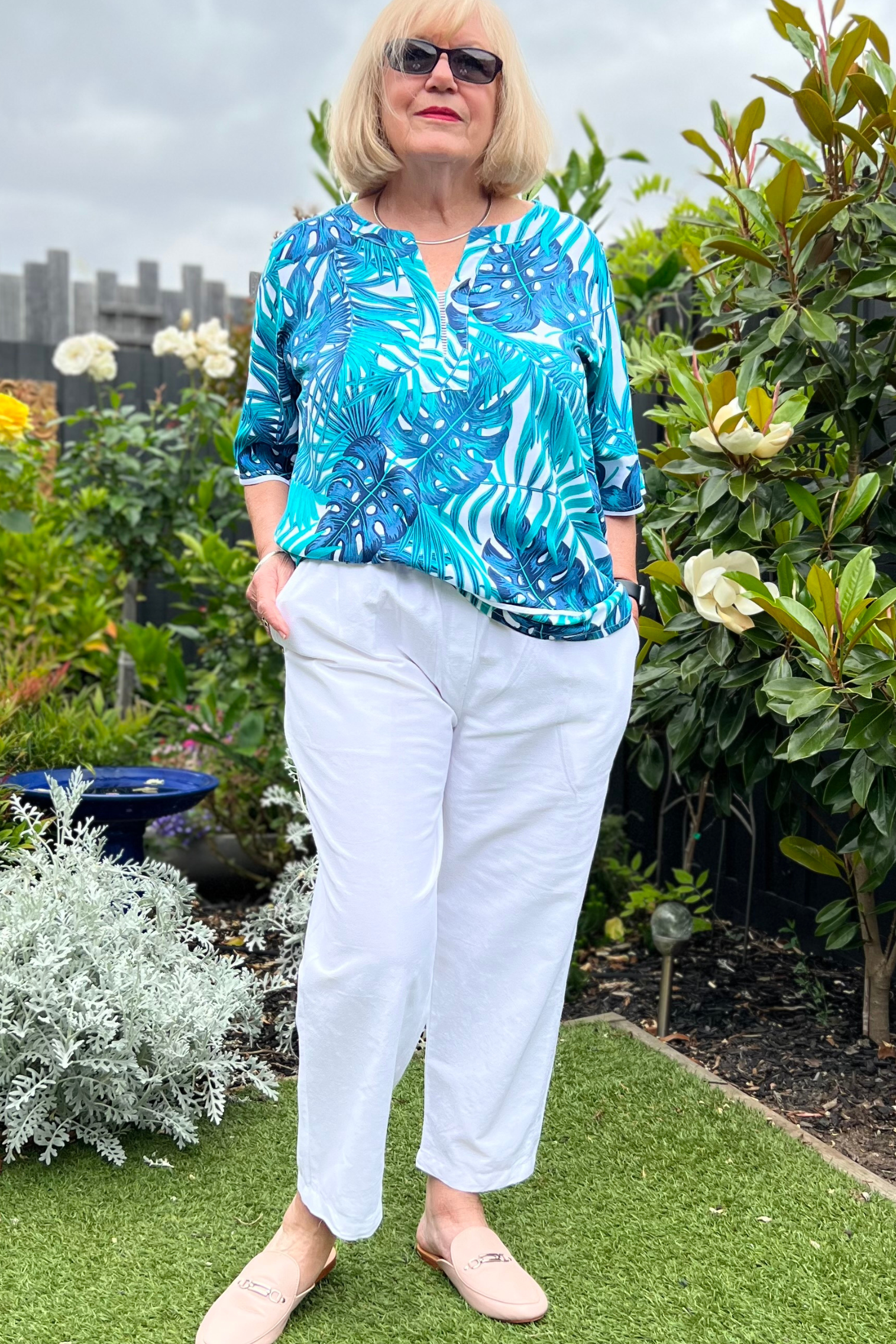 Kita Ku modelling the cotton white Pant Port with a tropical top in a garden setting. 