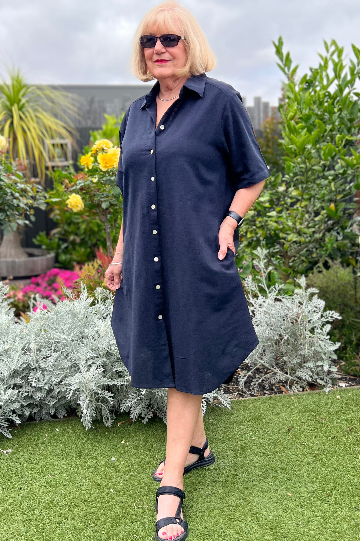 Kita Ku modelling the shirt dress pronto in solid black cotton and has shell buttons throughout, set in a sunny garden.
