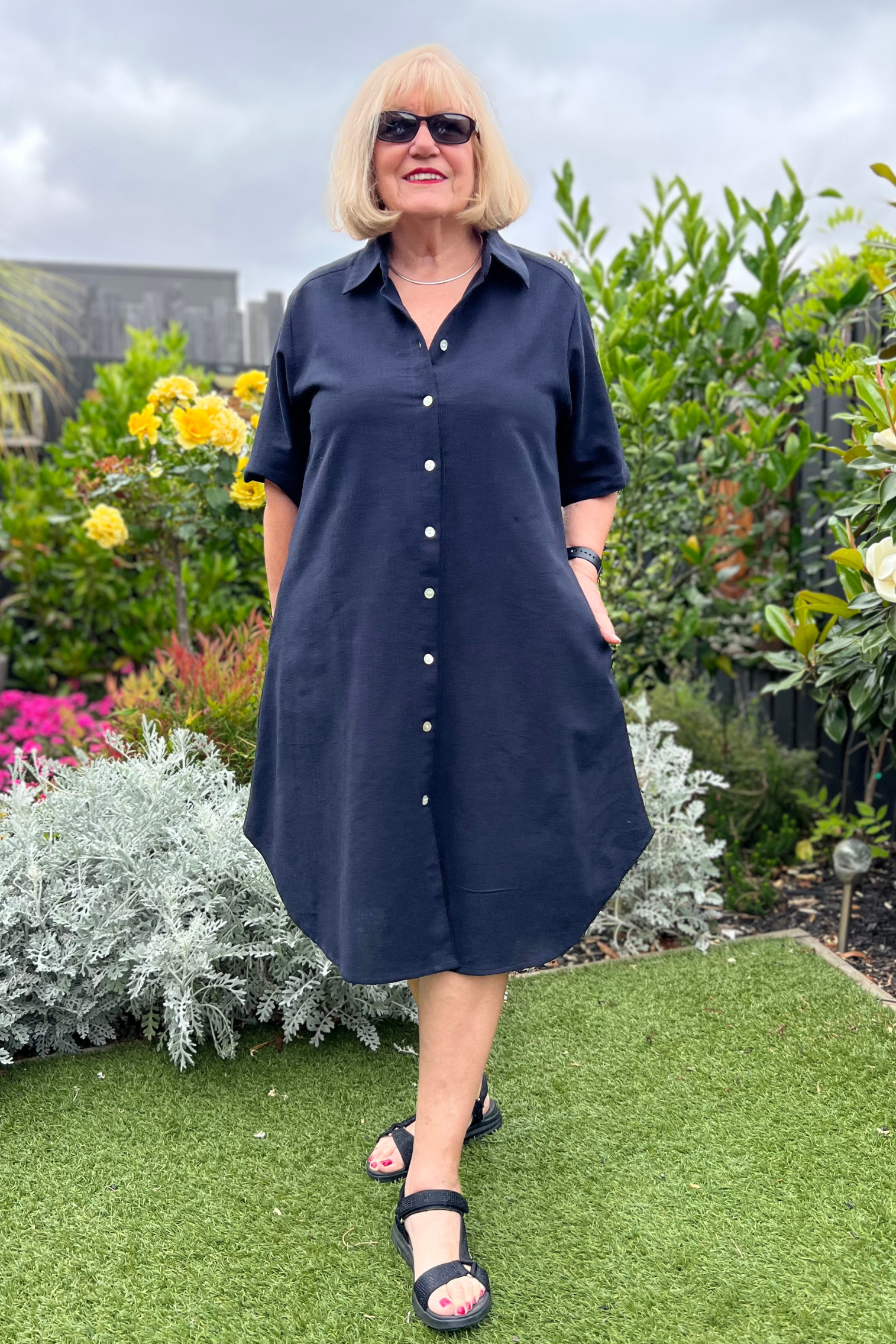 Kita Ku modelling the shirt dress pronto in solid black cotton and has shell buttons throughout, set in a sunny garden.