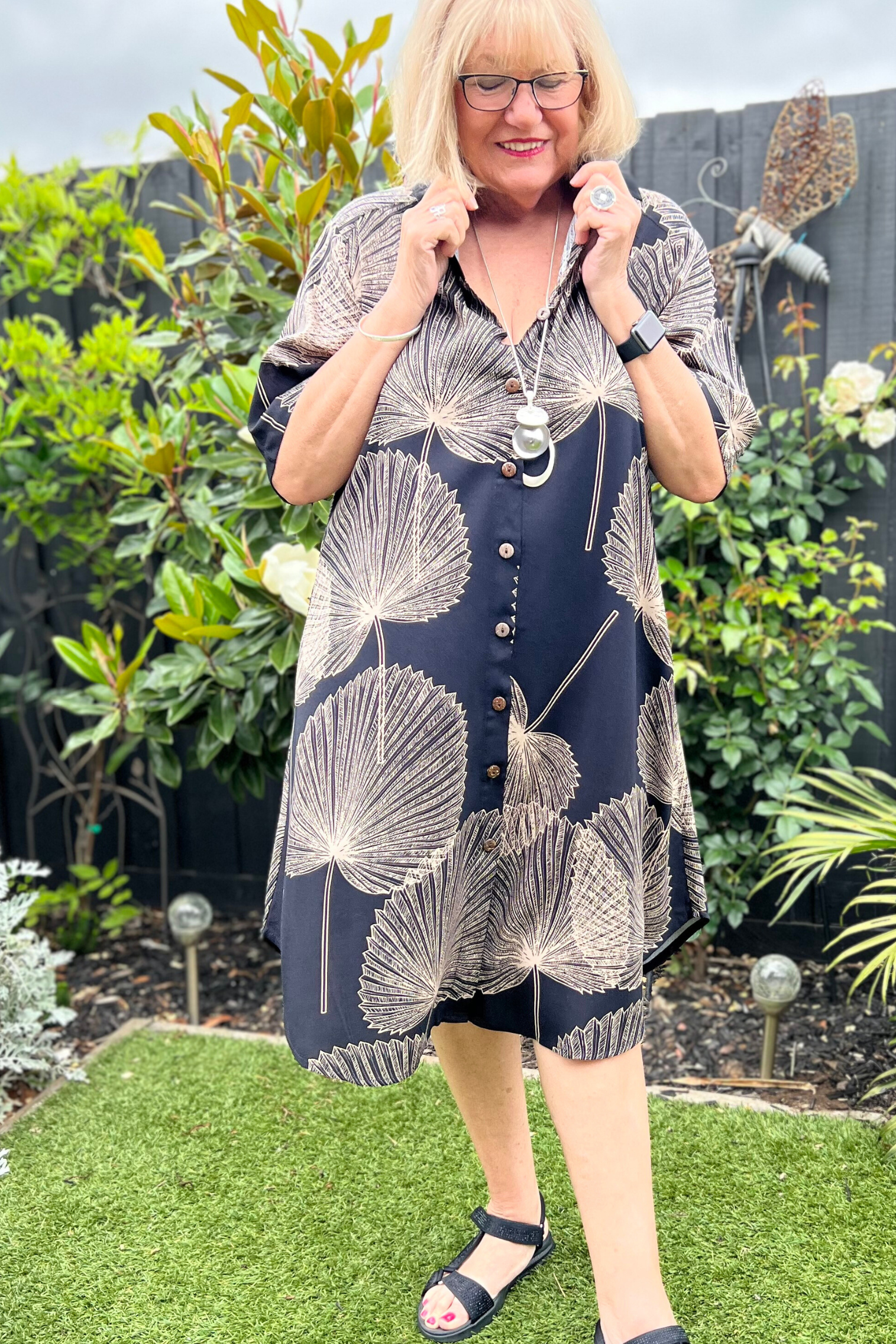 kita ku model in the shirt style dress pronto in a paolo print of fan black and mocha palm leaf set in a sunny garden.