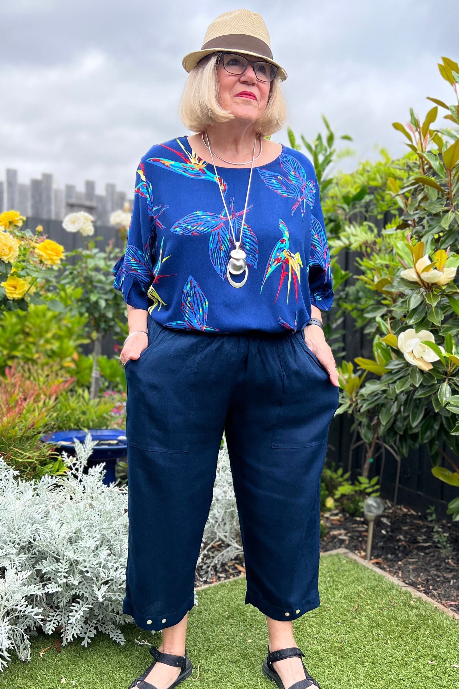 Kita Ku modelling a pant Sita in navy with button trim on the hem, also with a top Zara set in a sunny garden.