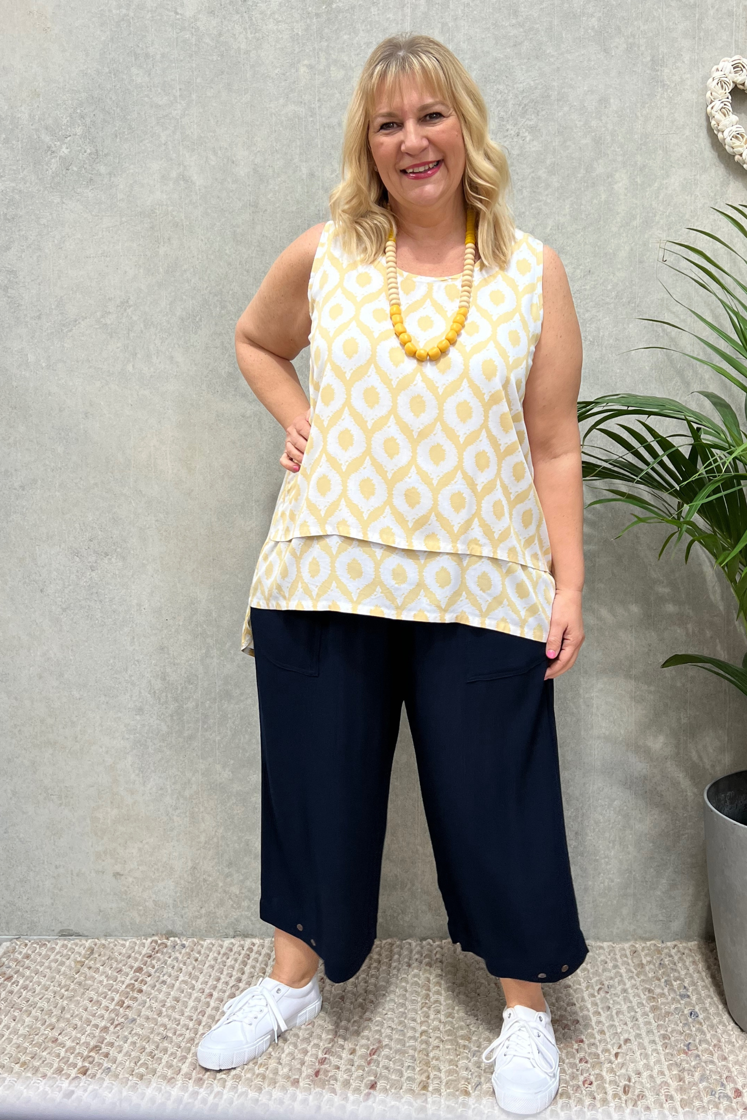 soft lemon shade layered no sleeve Tunic worn by Kita Ku blonde model  over navy wide pant and white sneakers.