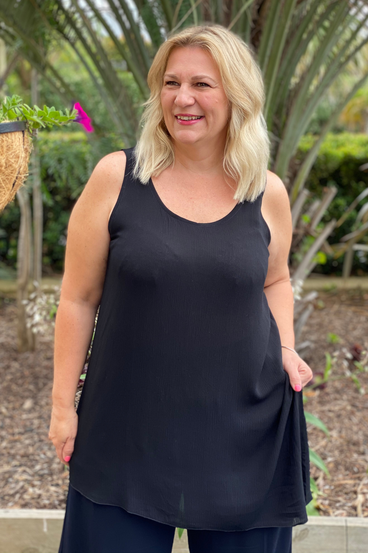 blond model in a garden setting with a longish black asymmetrical hemline tunic cami
